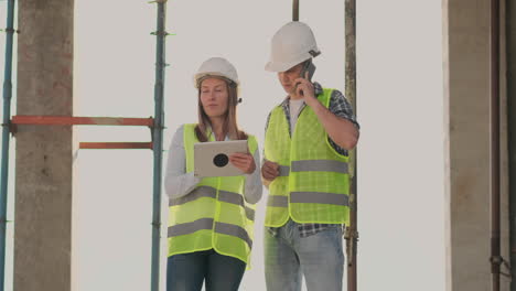 The-controller-is-a-man-of-a-building-under-construction-talking-on-the-phone-with-management-and-has-discussed-with-the-engineer-and-architect-woman-construction-progress.